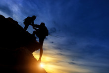 Silhouette Of The Climbing Team Helping Each Other While Climbing Up In A Sunset. The Concept Of Aid.