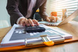 © NINENII - Male businessman working on desk office with using a calculator to calculate the numbers, finance accounting concept.