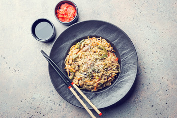 Wall Mural - Plate of wok or stir fry noodles with meat and vegetables over gray stone background, top view