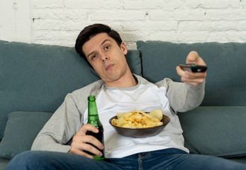 Wall Mural - Close up of bored young man sitting on the couch watching TV. Technology overuse concept