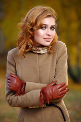 Stylish woman in beige coat and gloves standing in autumn yellow park.