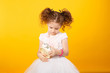 © Dragosh - Portrait of a little adorable curly girl, looking frowned on a alarm clock, over yellow background. copy space.