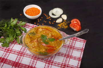 Wall Mural - Red lentil soup with tomatoes, onions, garlic and spices in a glass bowl with a spoon standing on a tablecloth on a black background