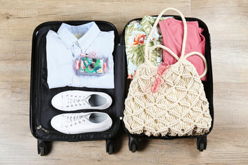 Wall Mural - Open suitcase fully packed with folded women's clothing and accessories on the floor. Woman packing for tropical vacation concept. Female luggage w/ things. Background, close up, copy space, top view.