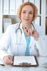 Wall Mural - Doctor woman at work. Physician filling up medical history records form at the desk. Medicine, healthcare concept