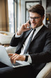 © Drobot Dean - Photo of pleased businessman using laptop computer and talking on smartphone in hotel hall