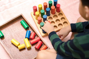 Closeup: Hands of a little Montessori kid (3-6) learning about size, orders, sorting, arranging by engaged colorful wooden sensorial blocks. Educational toys, Cognitive skills, Montessori activity.