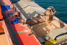 Loading Wheat On Cargo Ship With Crane And Bucket. Shipment From A Merchant Ship To A Small Ship. Grapple Crane Fill Wheat Into Cargo Ship.