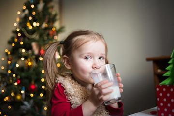 the child eats and drinks milk on the background of a Christmas tree with lights. children's xmas dinner