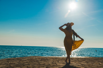 Wall Mural - young pretty smiling woman in yellow sundress walking by stone beach