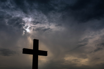 Silhouette of a simple catholic cross, dramatic stormclouds after heavy rain, copy space.