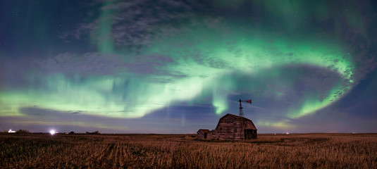swirl of bright northern lights over vintage barn, bins, windmill and stubble in saskatchewan, canad