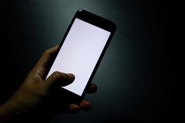 silhouette hand holding and touching a mobile phone with blank wihte screen in the dark darkness aga