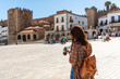 A young red-haired tourist with a backpack takes photographs of the Plaza Mayor in Caceres