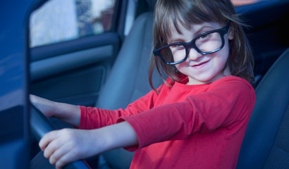 Driving shool. Humorous photo of happy cute little child girl in glasses learns to drive.