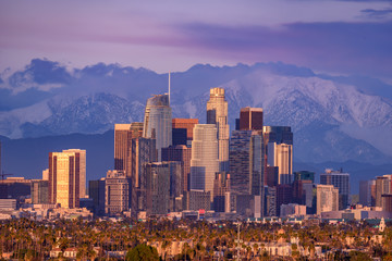 Downtown Los Angeles skyline with snow capped mountains behind at sunset