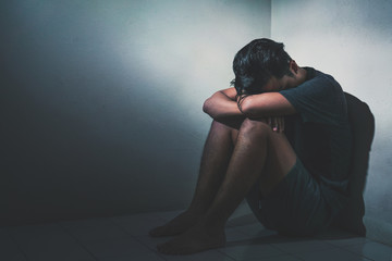 Young depressed asian man sitting alone in dark room  with low light environment, PTSD Mental health concept, Selective focus.