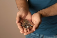 Young Man With Handful Of Coins On Beige Background, Closeup