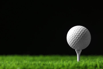 Golf ball with tee on artificial grass against black background, space for text