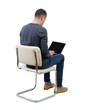 © ghoststone - Back view of a man who sits on a chair with a laptop.