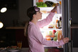 Beautiful young woman choosing food in refrigerator at night