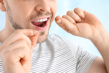 Wall Mural - Man flossing teeth on light background, closeup