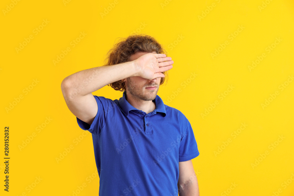 Young man covering his eyes on color background
