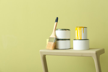 Cans of paint with brush on step ladder against color background