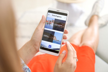 Woman with mobile phone visiting travel agency website at home