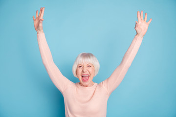 Portrait of cheerful modern lady raising arms shouting wearing pastel sweater isolated over blue background