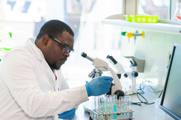 African-american scientist working in lab. Doctor making microbiology research. Laboratory tools: microscope, test tubes, equipment. Biotechnology, chemistry, bacteriology, virology and health care.