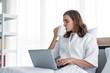 © P Stock - Young caucasian woman in white pajamas with white holding a cup of coffee and drink and find information from the laptop on a bed.