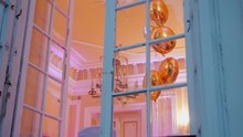 View From Vintage Window Of Old Palace To Festive Room With Golden Balloons, Chandelier And Beautiful Illumination At Night. Background Static B-roll 4K Video.