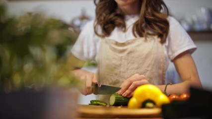 Wall Mural - Close up view of young woman hands cutting fresh vegetables on a wooden board for salad at the kitchen