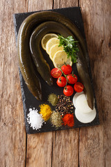 Wall Mural - uncooked fresh eel with spices, vegetables and lemon close up on a slate board. Vertical top view