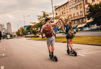 Young couple on vacation having fun driving electric scooter through the city.