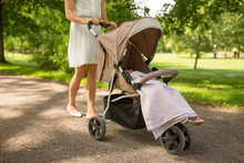 Family, Motherhood And People Concept - Mother With Child Sleeping In Stroller Walking At Summer Park