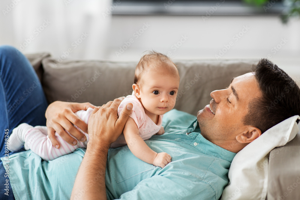 family, parenthood and fatherhood concept - happy smiling middle aged father with little baby daughter lying on sofa at home - obrazy, fototapety, plakaty 