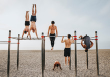 Fitness, Sport, Training, Calisthenics And Lifestyle Concept - Group Of Guys Training On The Beach Workout Bars