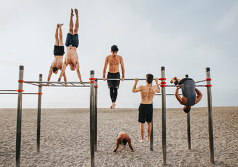 fitness, sport, training, calisthenics and lifestyle concept - Group of guys training on the beach workout bars