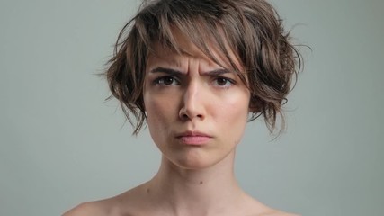 Canvas Print - Shocked young woman with natural skin getting angry while looking at the camera over grey background isolated