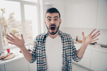 Portrait of his he nice attractive mad furious devastated bearded guy screaming in modern light white interior style kitchen