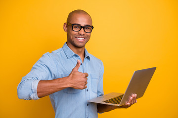 Photo of dark skin guy searching website notebook hold thumb raised up wear specs jeans denim shirt isolated bright yellow background