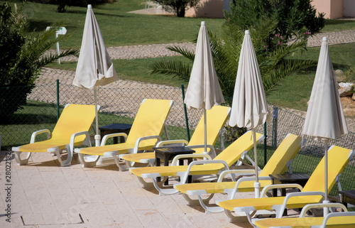 Some Yellow Deck Chairs And Umbrellas Nearby A Pool In A