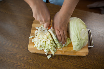 Female hands cut cabbage on a wooden plate on the table in the kitchen. Proper nutrition.