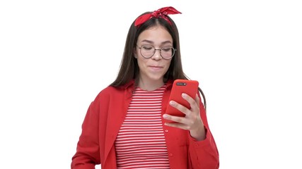 Sticker - Cheerful young girl in red shirt smiling and making winner gesture while using smartphone over white background isolated