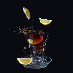 Transparent cups with tea on a black background. Lemon slices fall into the cup. Bursts, splashes.