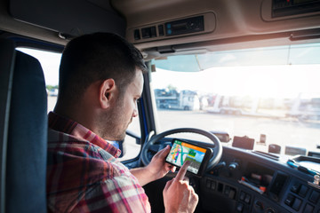 Professional middle aged trucker using truck gps navigation to transport and deliver goods to the destination. Transportation services.