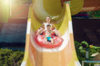 European boy and mother slides down water slider on floater at waterpark.