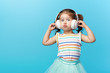 © oes - Happy smiling child enjoys listens to music in headphones over colorful bleu background. Vivid and fun emotions, happy child with pleasure listens to songs in wireless headphones